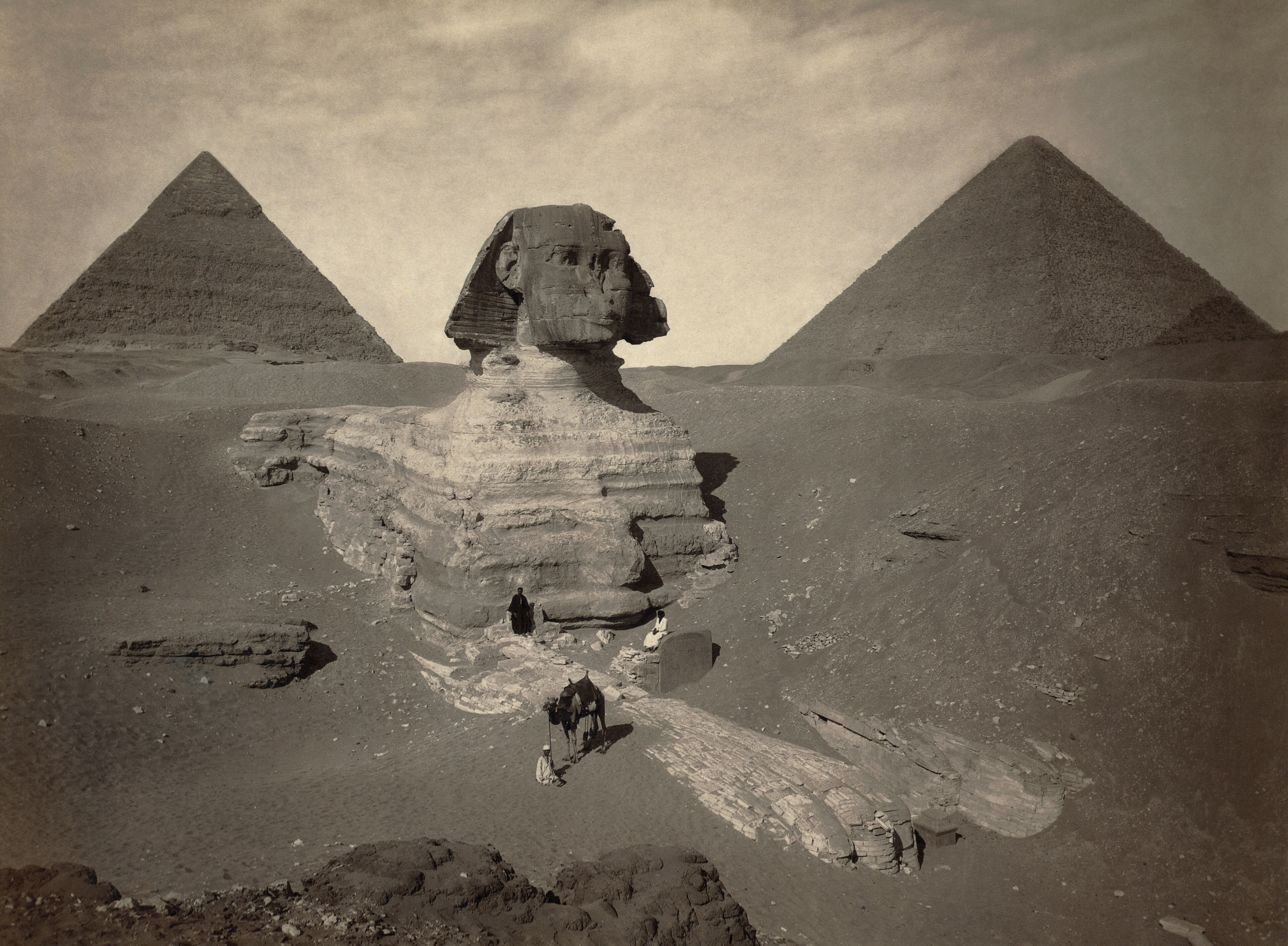 أبو الهول بالجيزة وقد أُزيح الرمل جزئياً عن جسده وفي الخلفية هرم، في صورة فوتوغرافية من القرن التاسع عشر