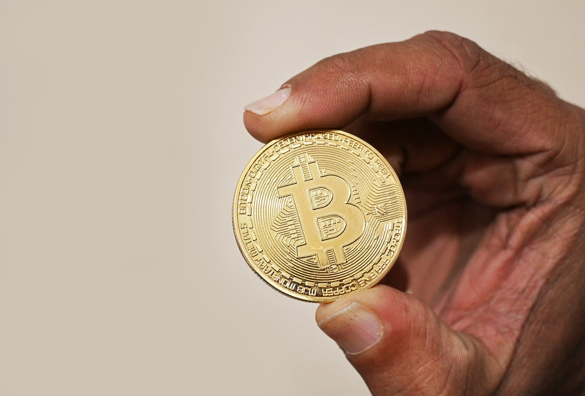 A hand holding a gold-coloured physical bitcoin medallion