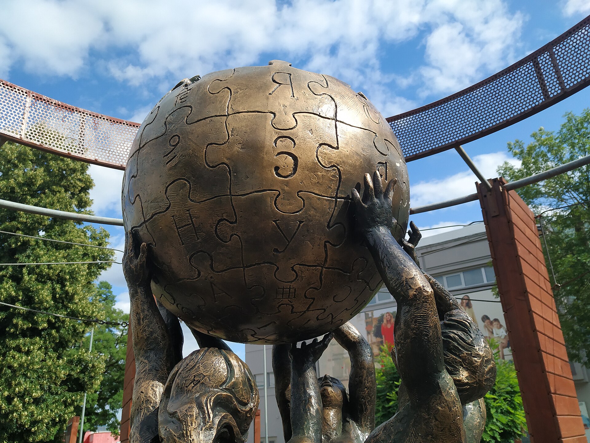 The Wikipedia Monument in Słubice, Poland: bronze figures raising the Wikipedia puzzle-globe against a blue sky